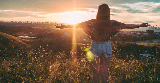 forgiving person standing on hilltop arms open looking at cityscape horizon at sunset feeling free released