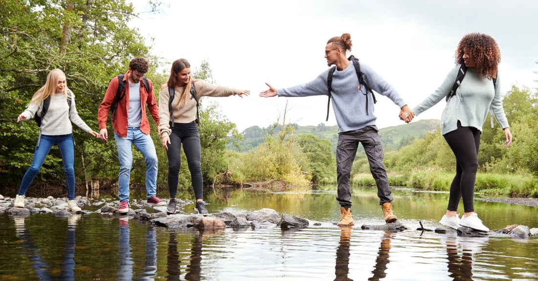 group of friends hiking crossing creek generously assisting each other across on rocks