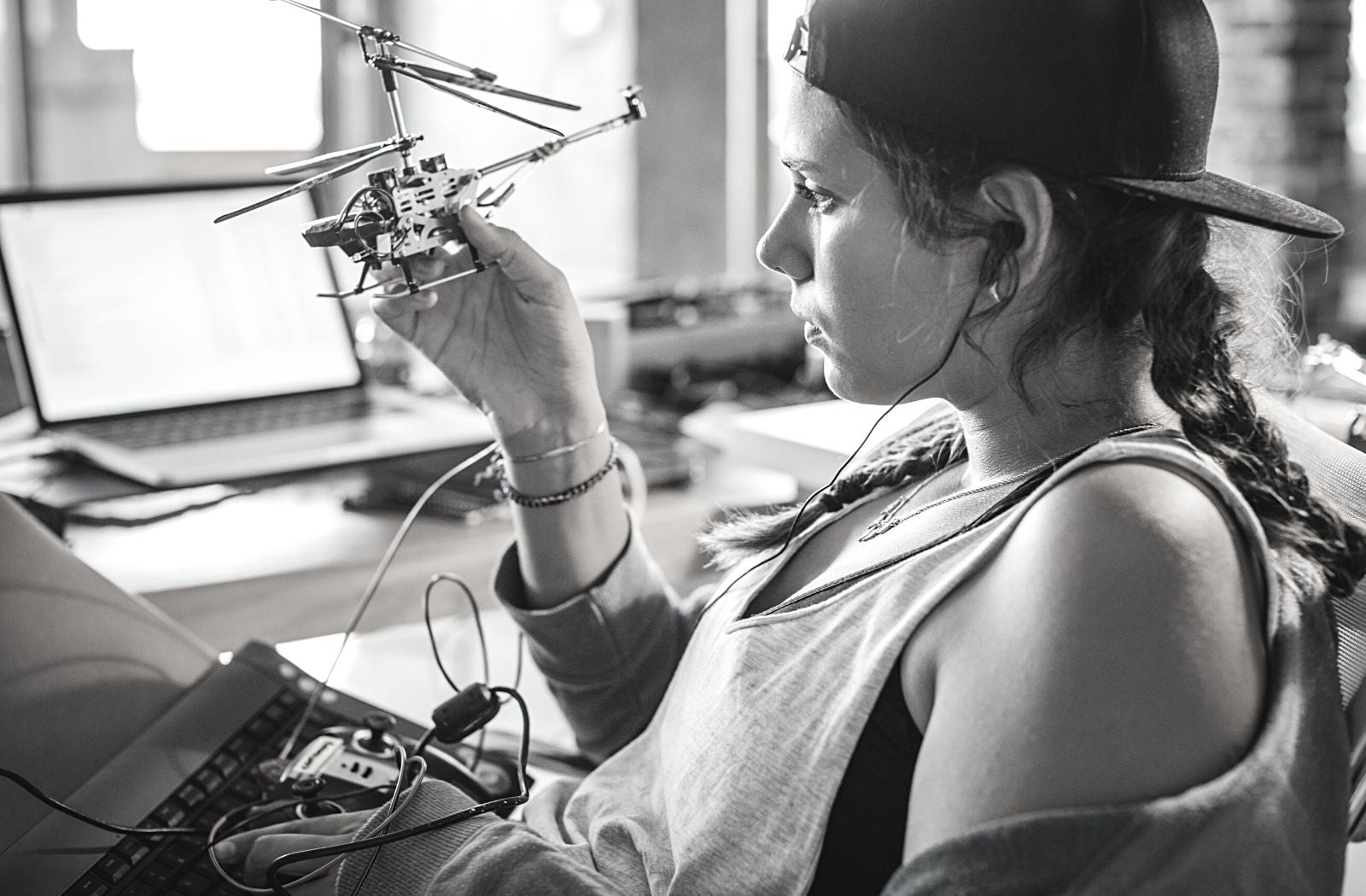 curious young woman with long braided hair wearing cap backward holding reviewing helicopter model engineering project