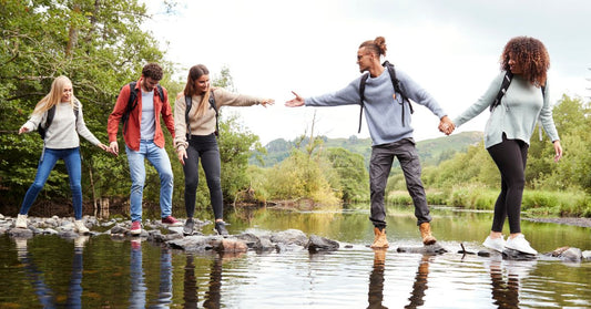 group of friends hiking crossing creek generously assisting each other across on rocks