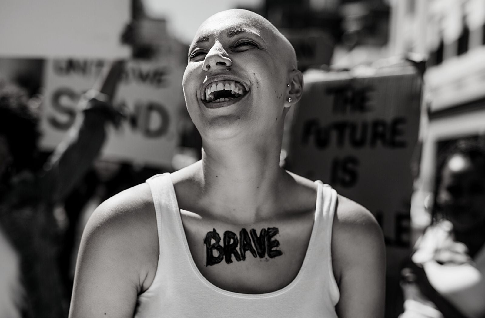 brave bald woman laughing wearing white tank top outdoors during civil protest