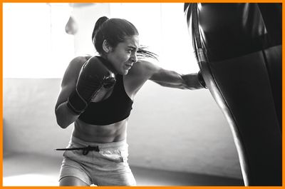 Female-boxer-hitting-punching-bag-left-hook-in-boxing-studio-training-hard-with-determination