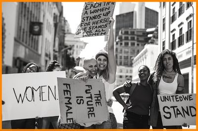 Six women peacefully protesting for women empowerment equality fair treatment holding signs standing in city street