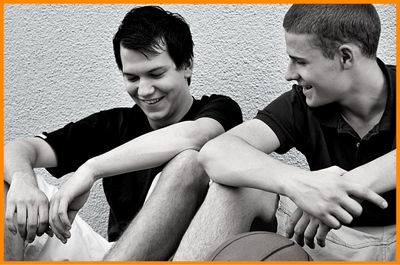 Two friends young men sitting next to each other smiling trash talking about basketball game they just played