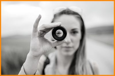 young woman holding up camera lens looking through it on country road