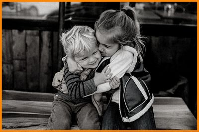 brother sister little children sitting on bench hugging each other smiling in playful loving way