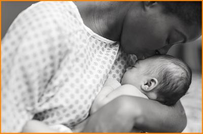mother-wearing-hospital-gown-holding-newborn-baby-child-to-her-breast-kissing-baby-head