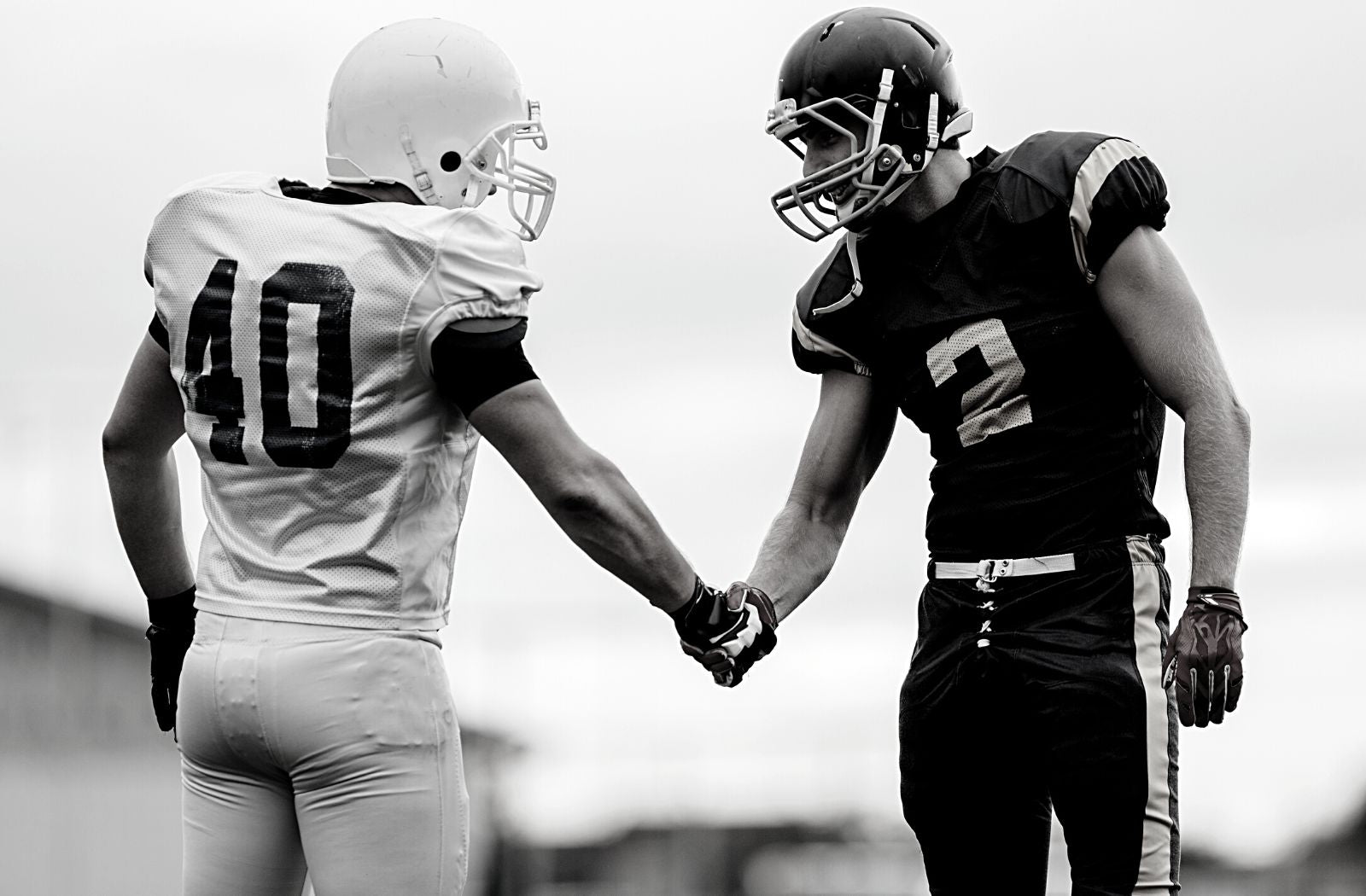 two American football players in uniform being fair person shake hands after playing game